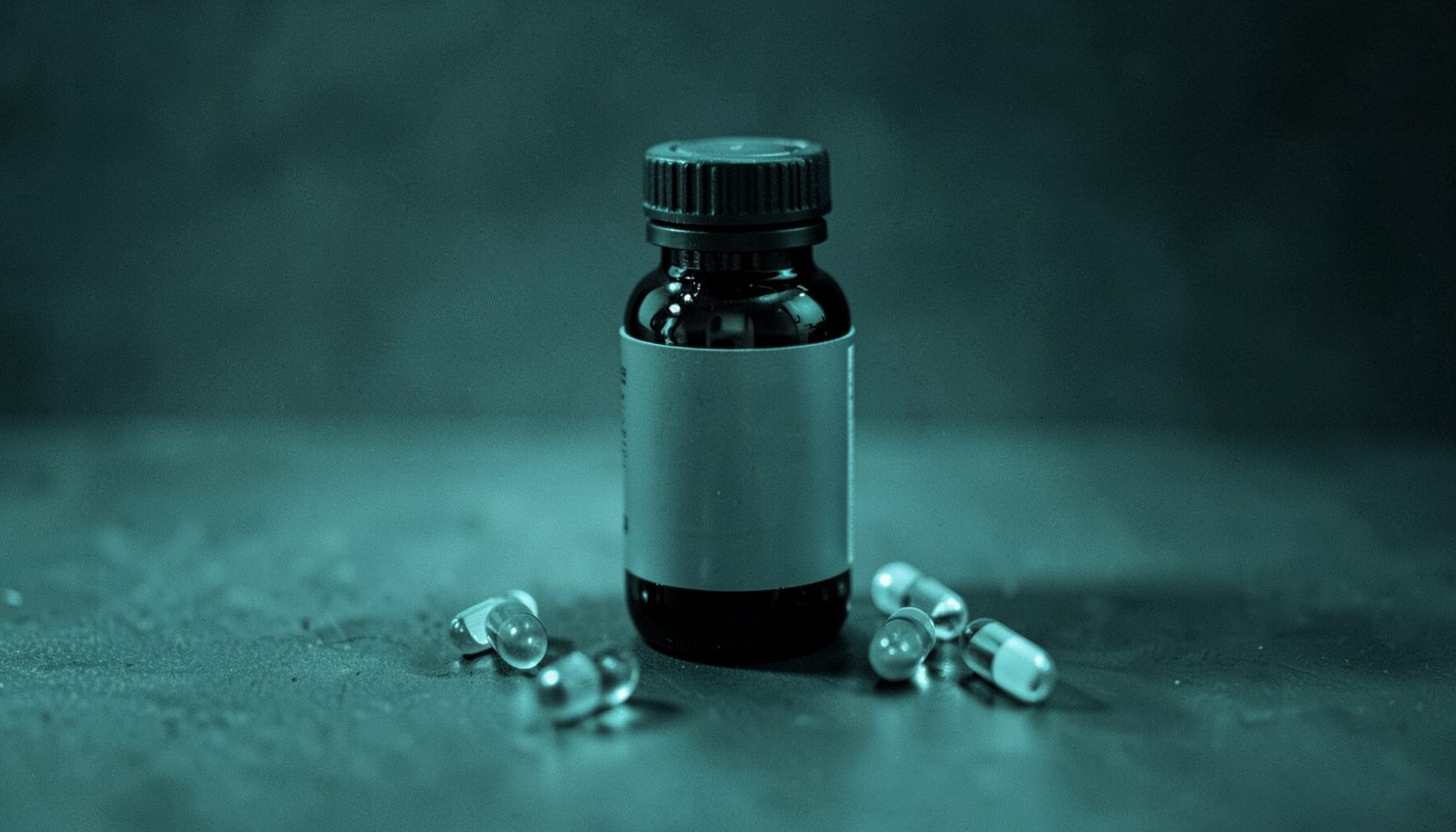 Duotone photograph of a small amber supplement bottle with capsules scattered nearby, dark clinical mood