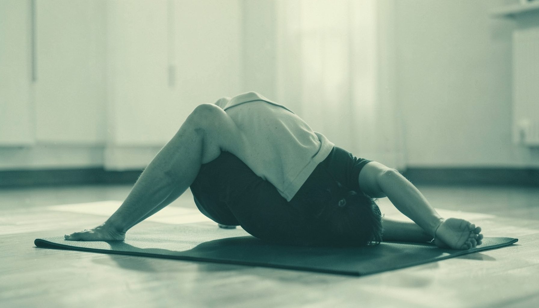Duotone photograph of a person practicing yoga on a mat in soft morning light, muted sage and cream tones, serene and grounded mood