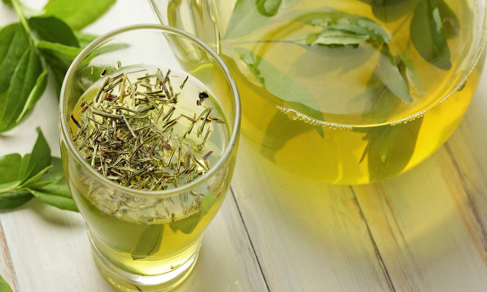Glass and pitcher of green tea with fresh leaves on a wooden surface, yellow-green tones, calm and fresh mood